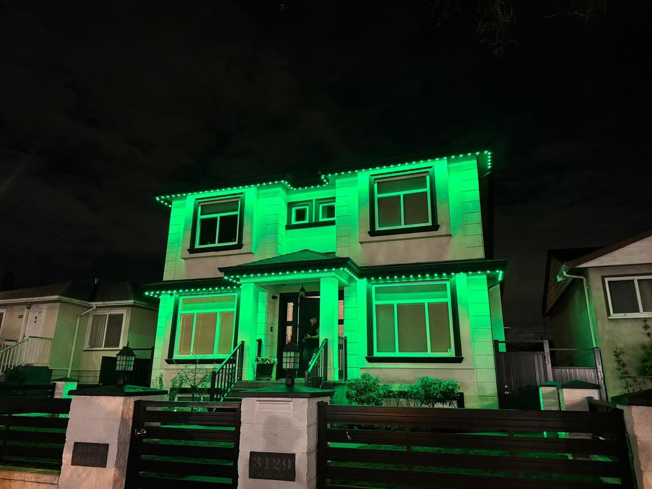 A two-storey Vancouver home with its rooflines, gables and porch outlined in colour-changing LED lighting.