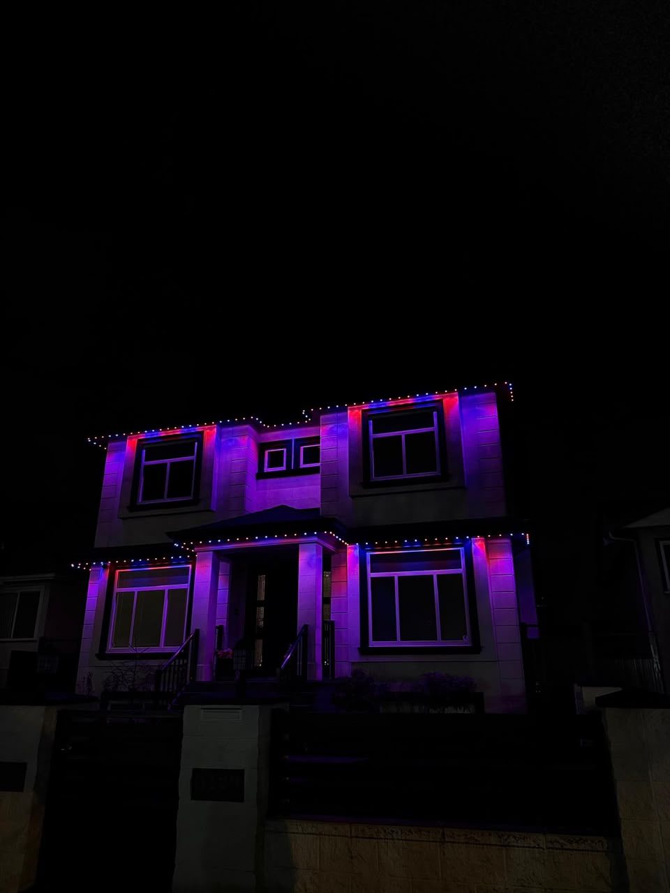 A home lit in a violet and ruby gradient across every roofline at night.