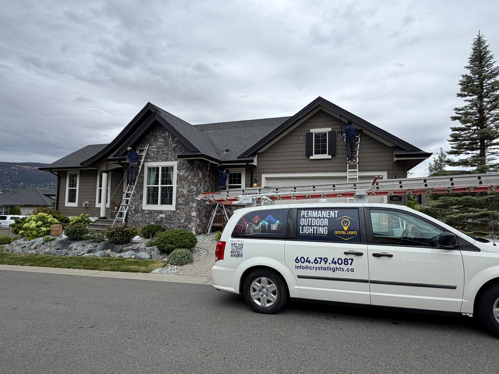 Crystal Lights technicians installing track on a home, with the company van parked out front.